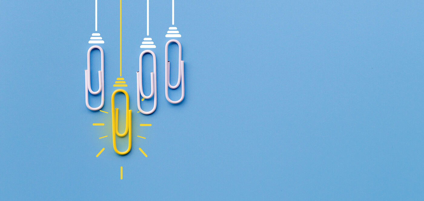 Paper clips hanging on a blue background, one of them yellow